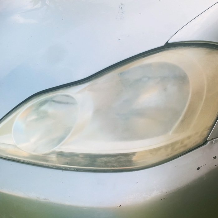 Cloudy and oxidized car headlight before restoration on a silver vehicle.