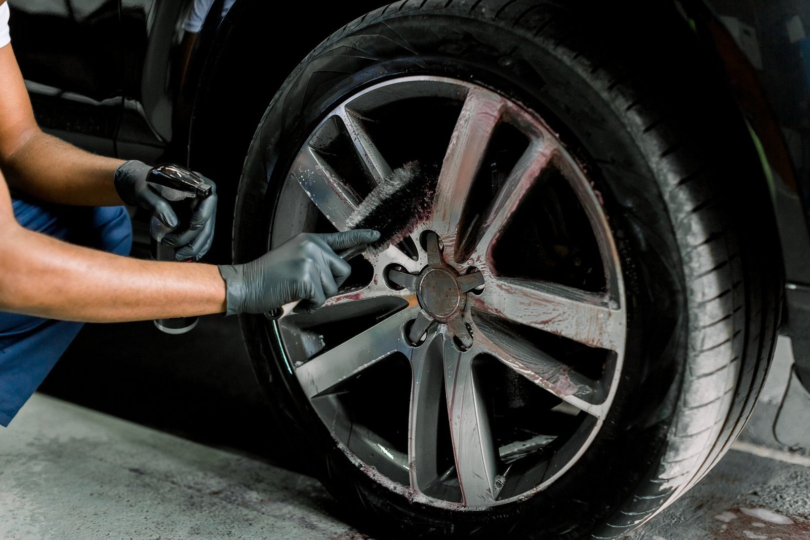 Detailer cleaning car rims with a brush during a wheel detailing service.