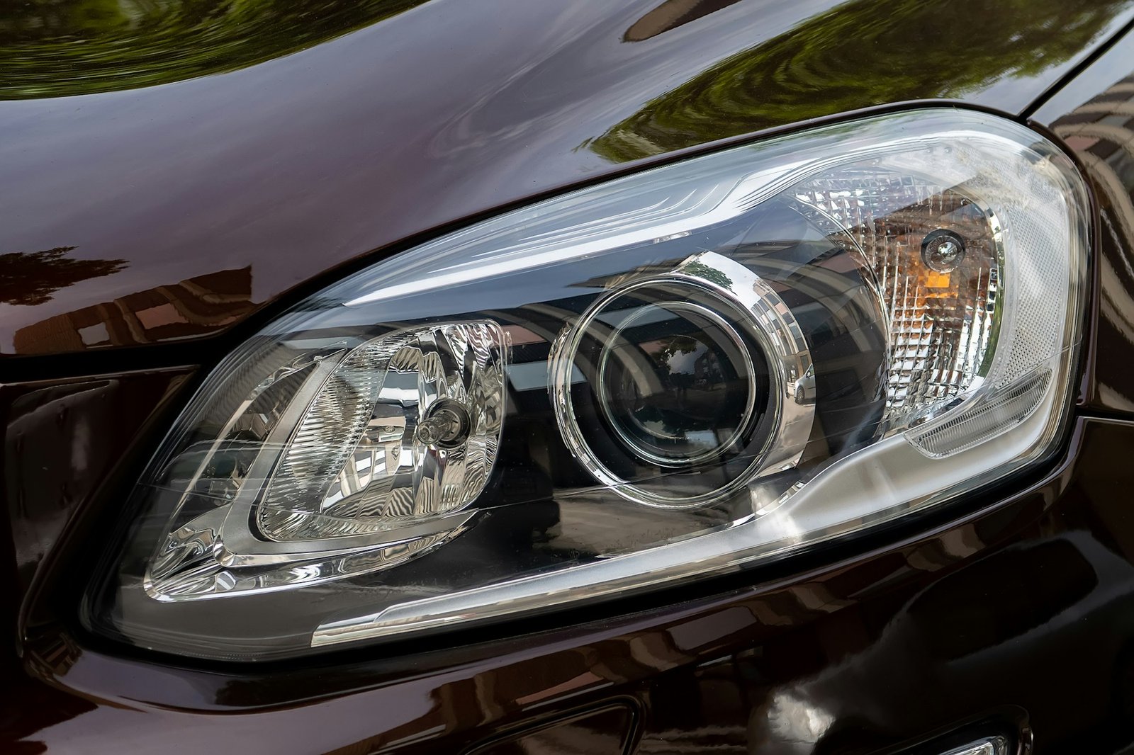 Close-up of a polished headlight on a dark-colored vehicle after a detailing service.