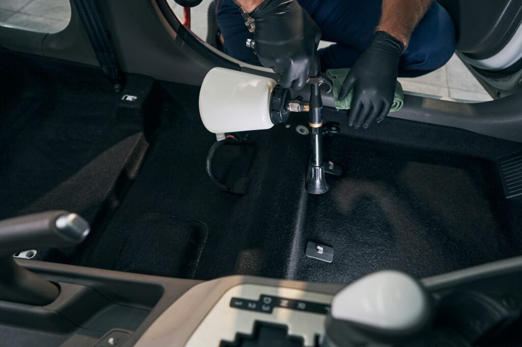 Detailer using a foam sprayer to clean the interior carpets of a vehicle.