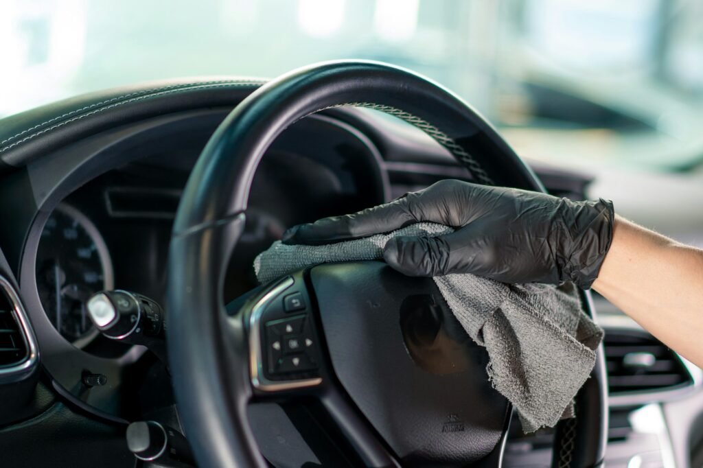 Detailer wiping down a car’s steering wheel with a microfiber cloth during an interior cleaning service.