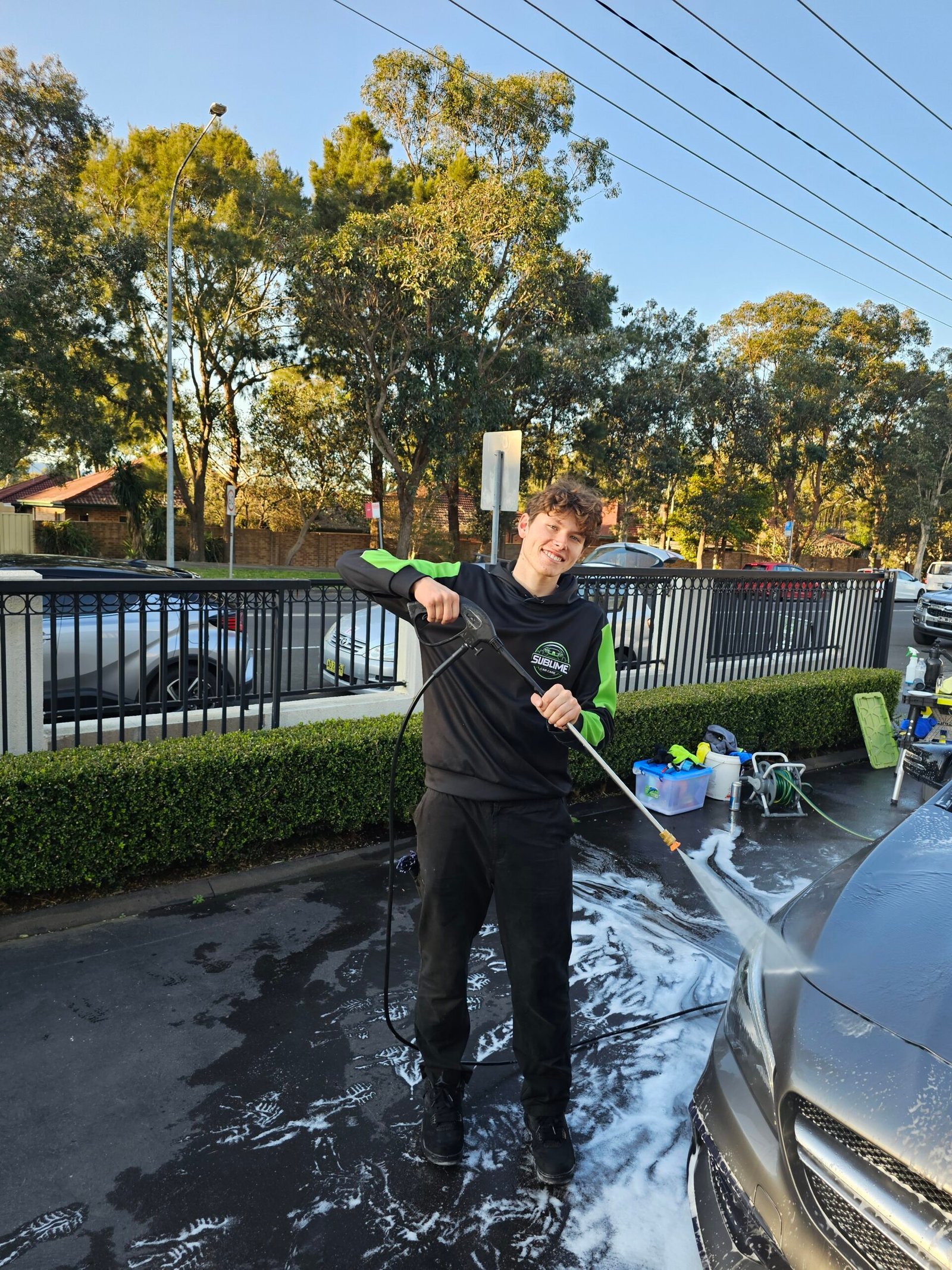 Detailer smiling while pressure washing a car in an outdoor setting.