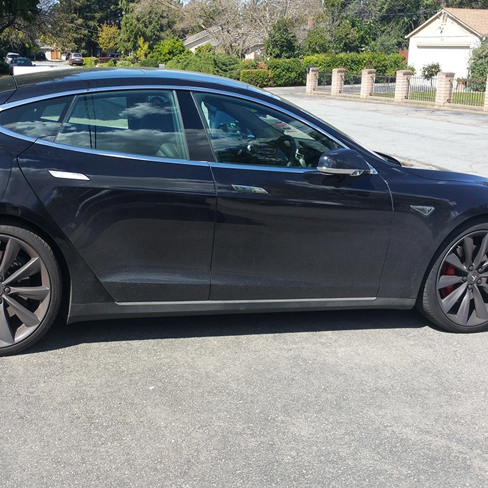 Side view of a black Tesla parked on a street before a detailing service.