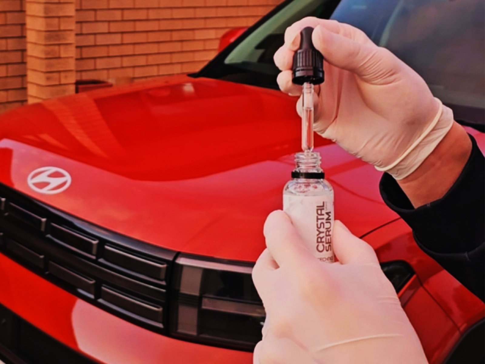 Detailer applying a ceramic coating with a dropper in front of a red Hyundai.