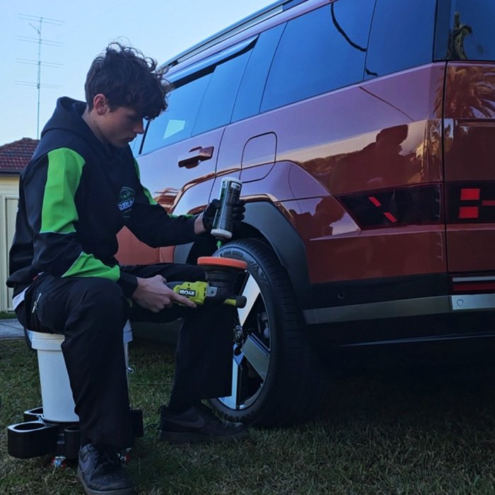 Detailer preparing a polishing machine for use next to a red SUV during a detailing service.