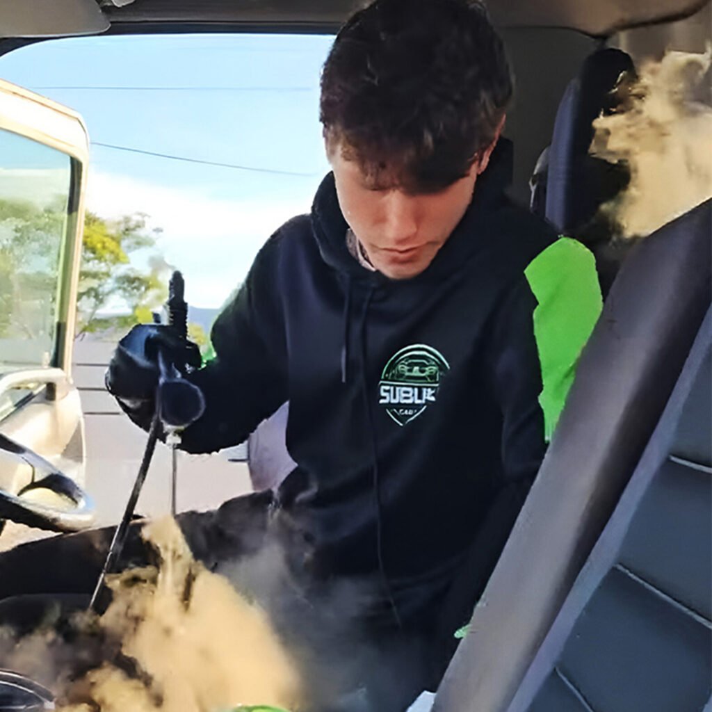 Detailer using a steam cleaner on a car seat during a detailing service.