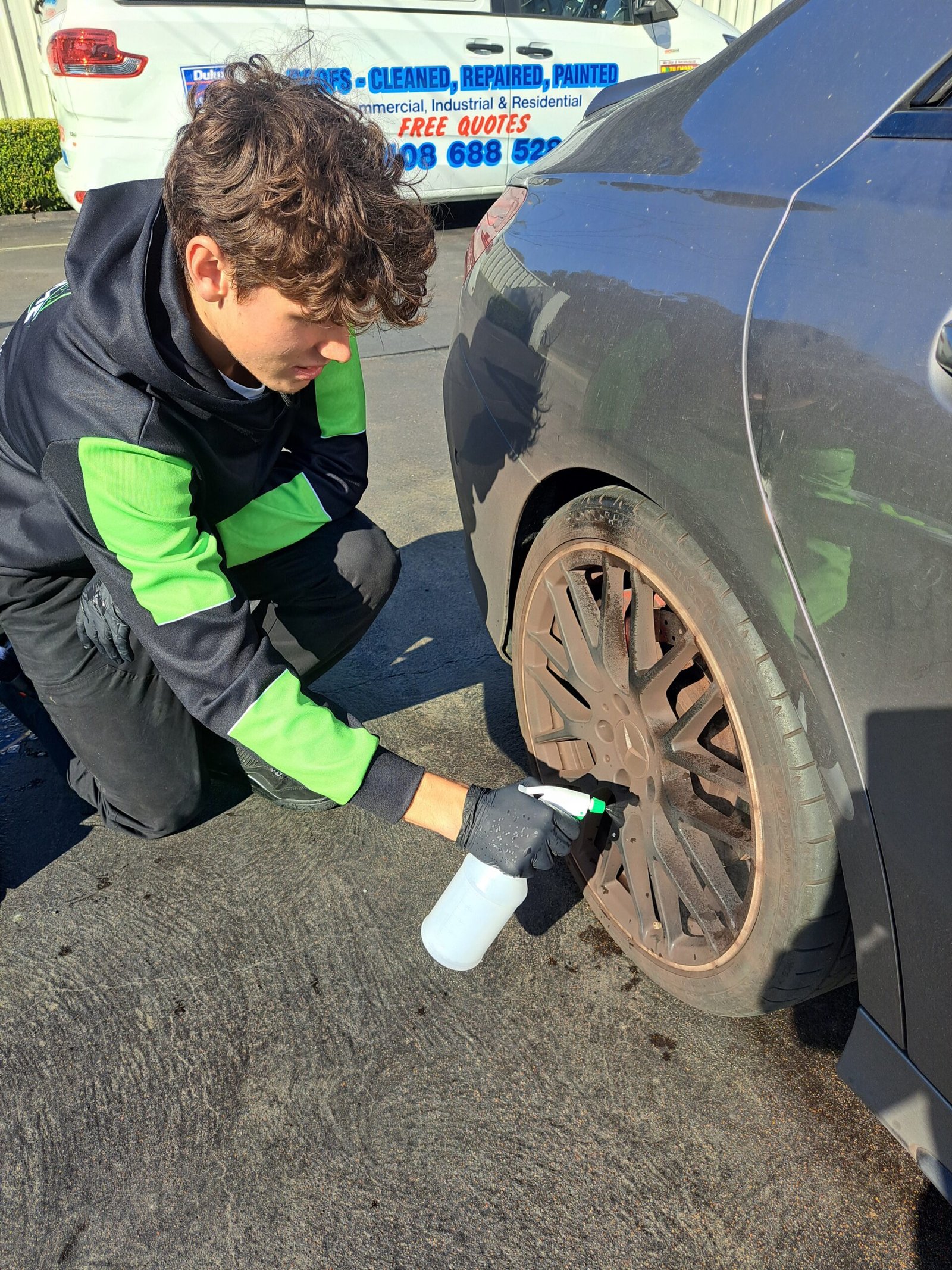 Detailer applying cleaning solution to dirty car rims during a detailing service.