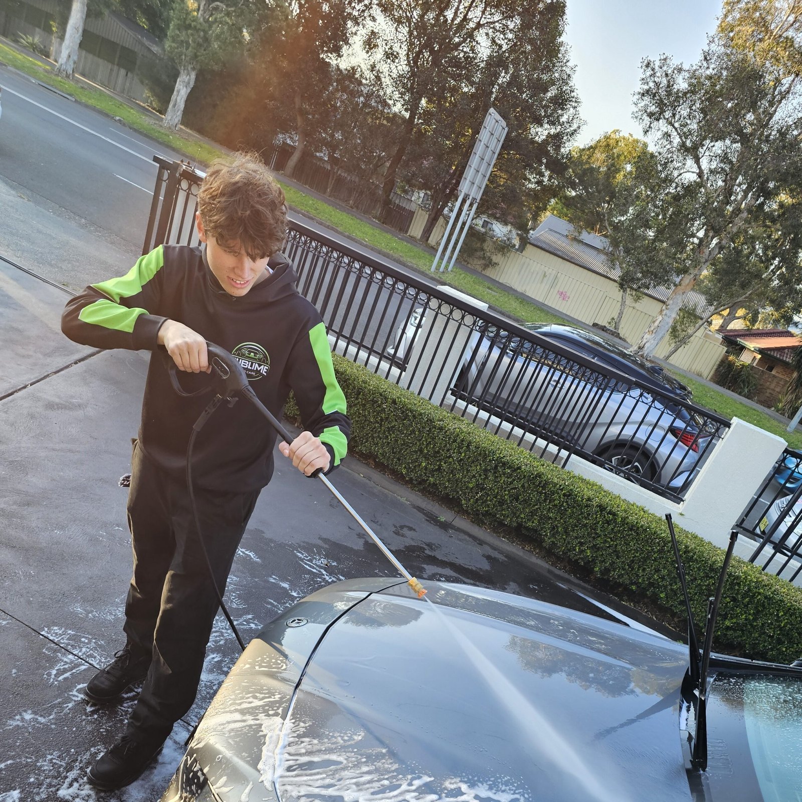 Detailer pressure washing the hood of a car during an outdoor detailing service.