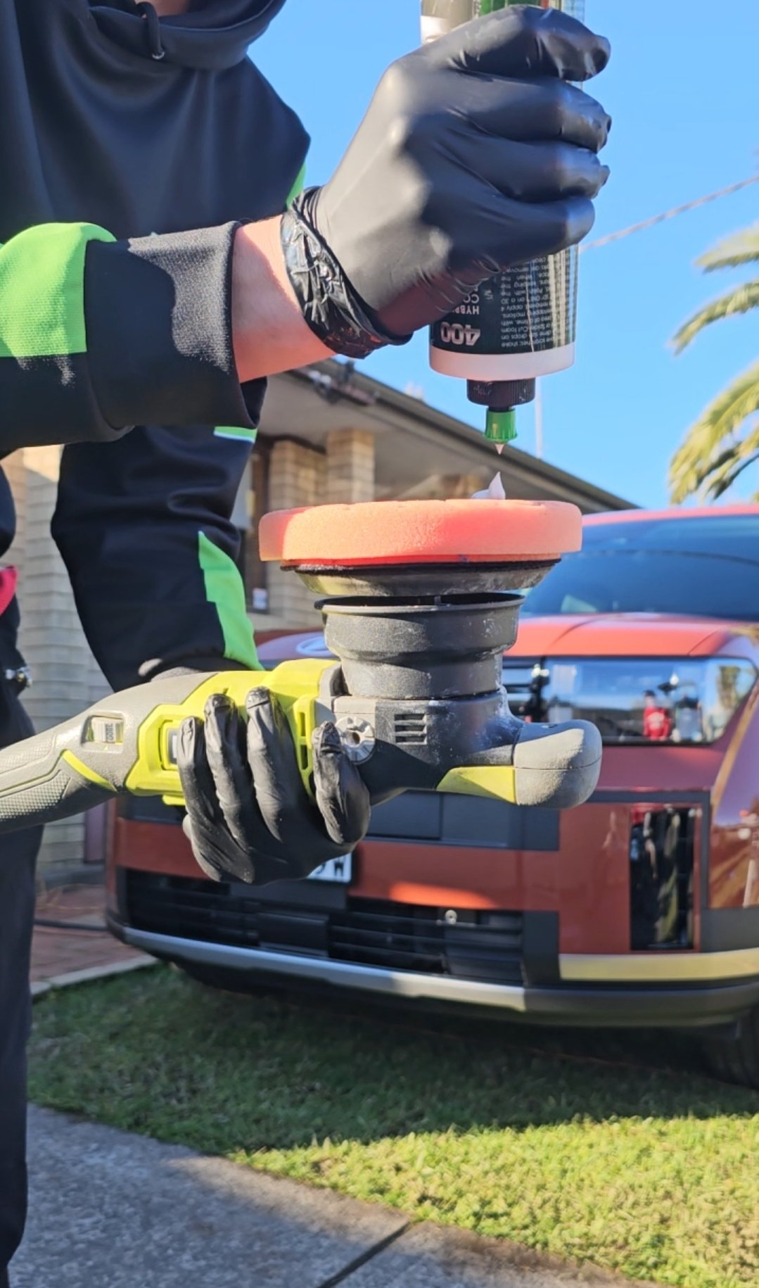 Detailer applying polish to a buffer machine in front of a car.