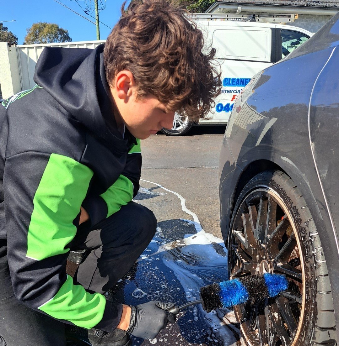 Detailer cleaning car rims with a brush during a detailing service.