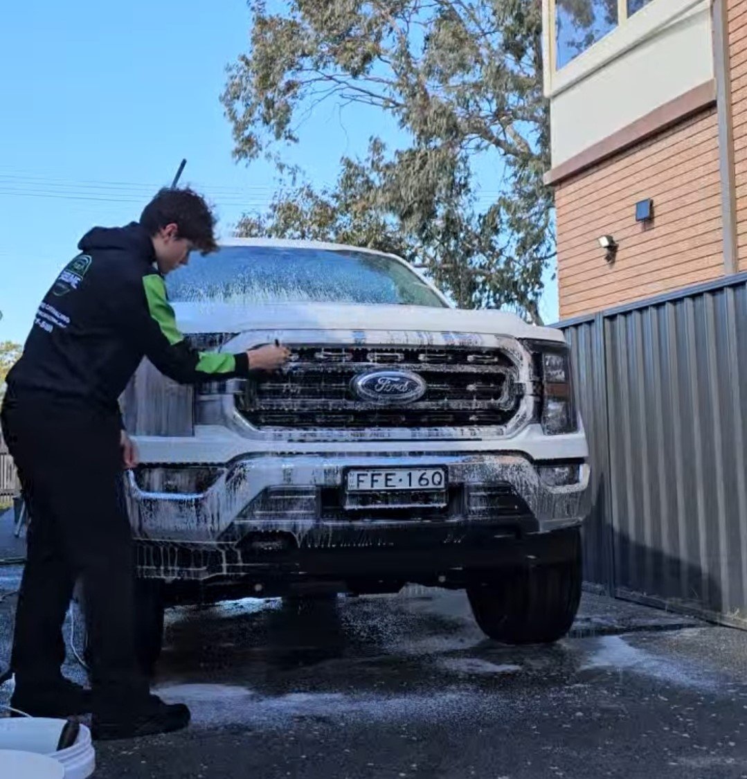 Person washing a white Ford truck with foam at Sublime Car Care.