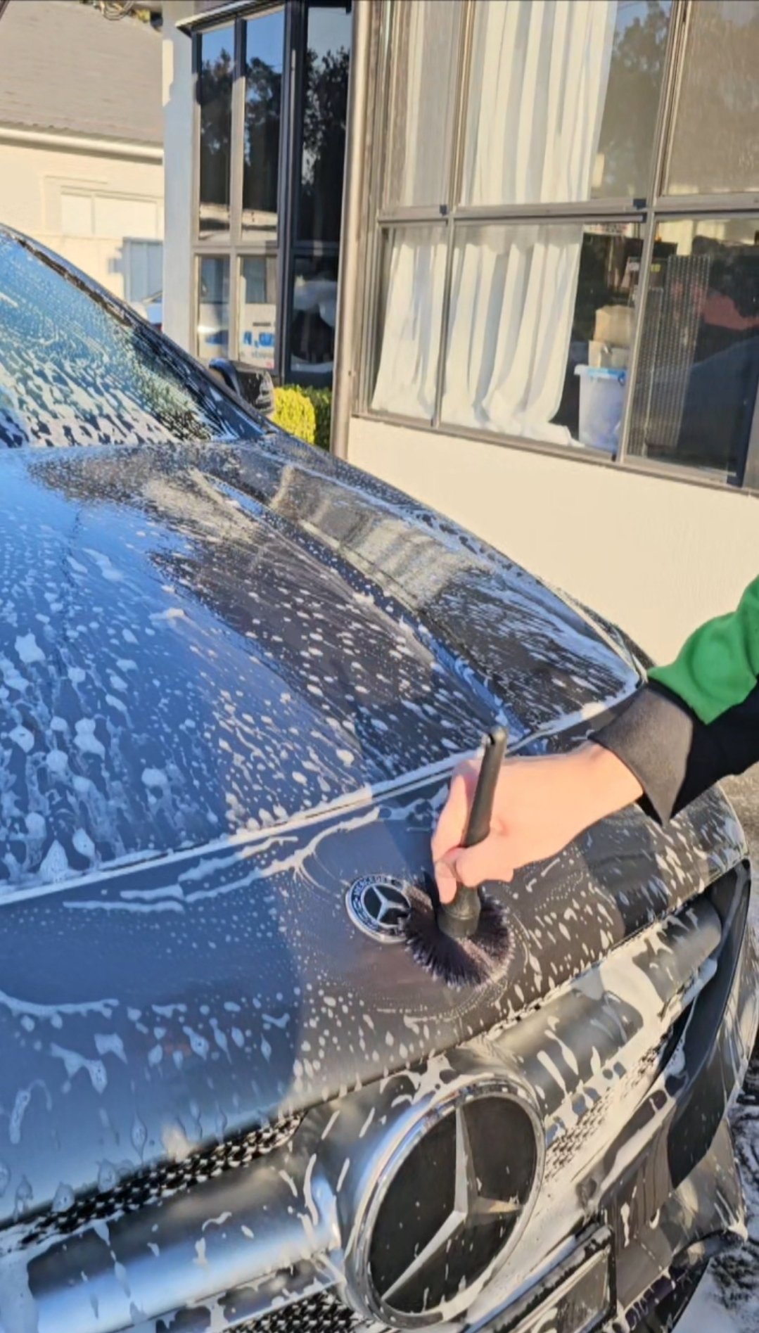 Close-up of a Mercedes-Benz being hand-washed with foam by a detailer.