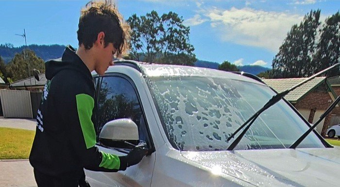 Detailer cleaning the windshield of a white vehicle during a detailing service.