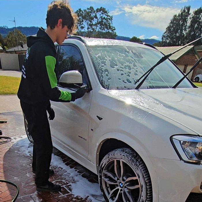 Detailer washing a white BMW SUV with foam during a detailing service.